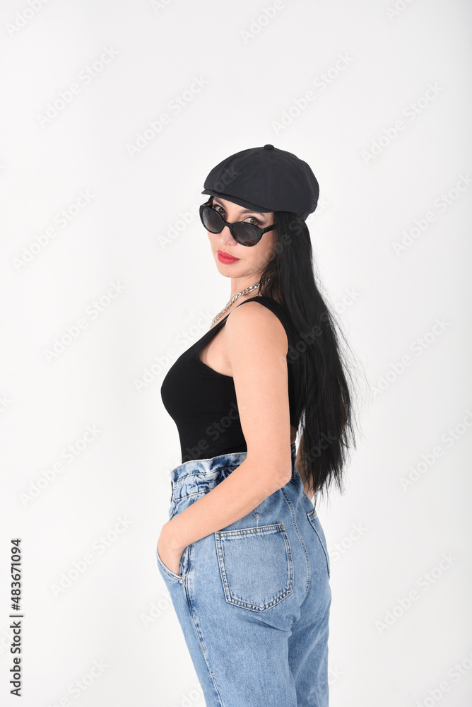Stylish woman in the studio on a white background in sunglasses, jeans and a black T-shirt and a black cap Stylish woman in the studio on a white background in sunglasses, jeans and a black T-shirt and a black cap