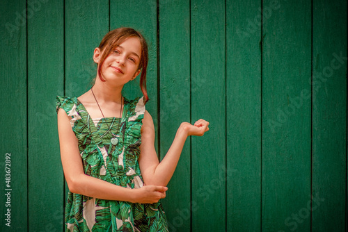 Teen girl portrait in a dress on a green background. Girl 10 or 11 years old on a summer day. photo