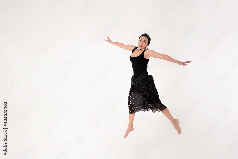 A brunette woman in a black dress barefoot jumped into the air in delight on a white background A brunette woman in a black dress barefoot jumped into the air in delight on a white background