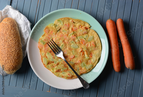 omelette with carrots and zucchini in the big plate with the bread beside it #483674471