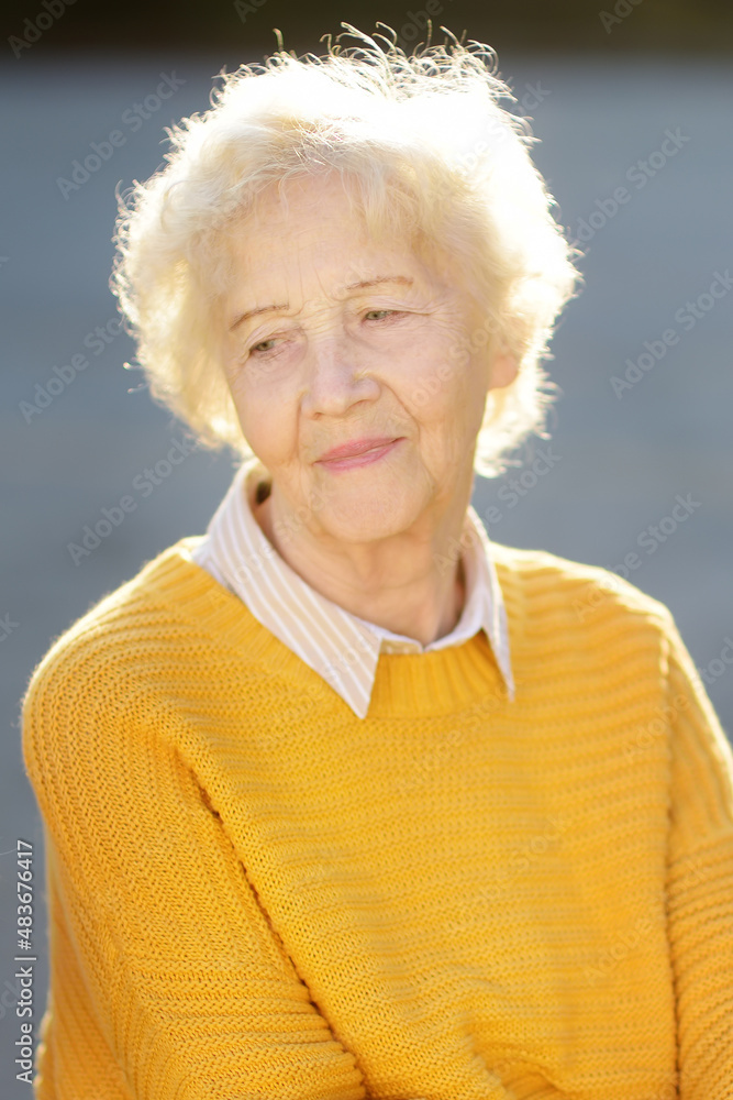 Outdoors portrait of beautiful smiling senior woman with curly white hair. Elderly lady walking in autumn park. Active longevity Outdoors portrait of beautiful smiling senior woman with curly white hair. Elderly lady walking in autumn park. Active longevity