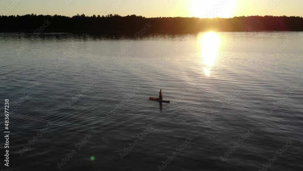 Aerial view of a man using his paddleboard in a lake during sunset. Aerial view of a man using his paddleboard in a lake during sunset.