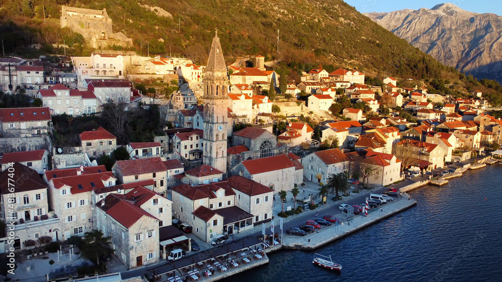 Breathtaking panoramic sunset aerial drone view of the ancient city of Perast, Montenegro. Old medieval little town with red roofs and with majestic mountains on background.