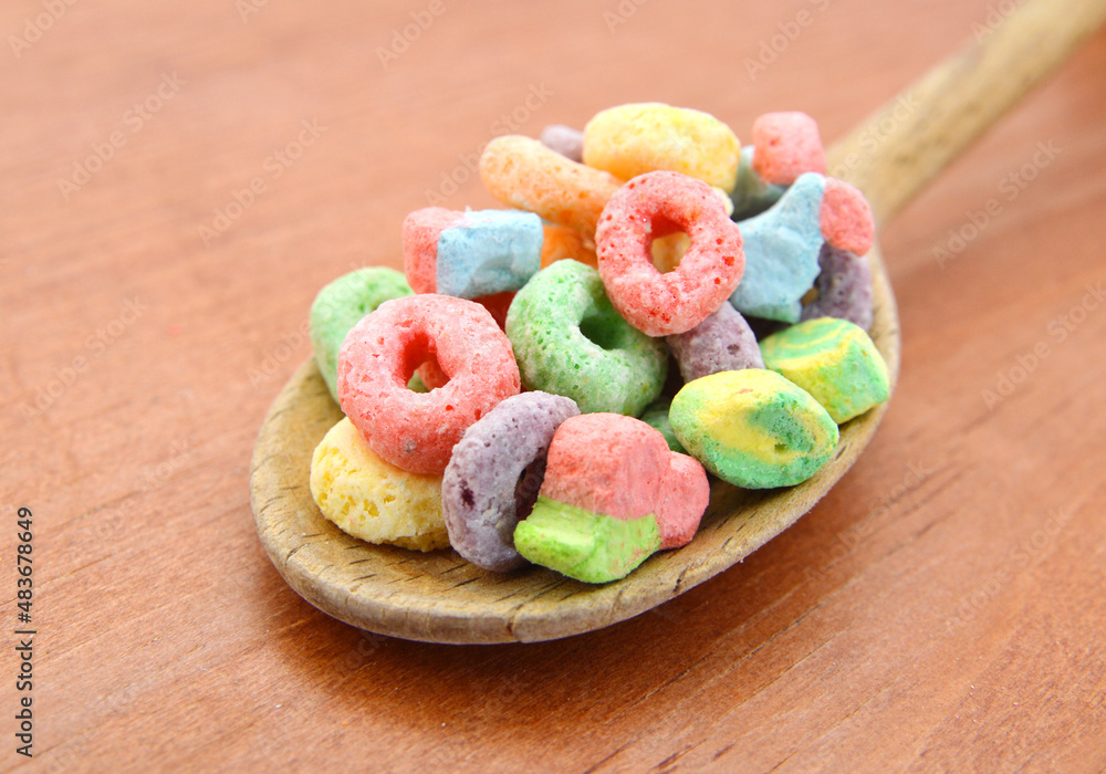 Delicious and nutritious fruit cereal loops flavorful in wooden spoon on wooden board, healthy and funny addition to kids breakfast