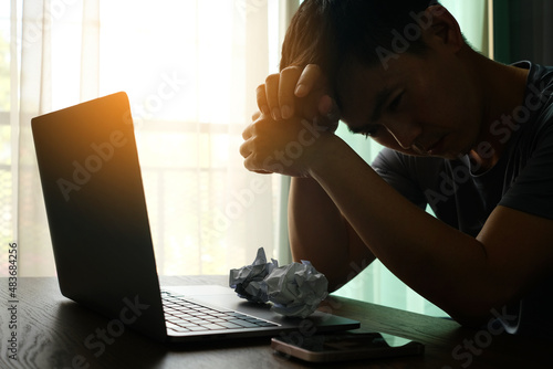 The man sitting down, his face unsettled. At the computer desk, she has headaches and stress. Cause of hard work and insufficient rest. photo