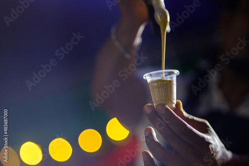 Manos de hombre afrodescendiente sirviendo espuma de cafe en un vaso pequeño descartable en una feria photo