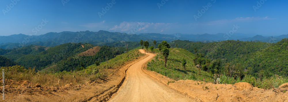 Panoramic view of dirt road in countryside with blue sky