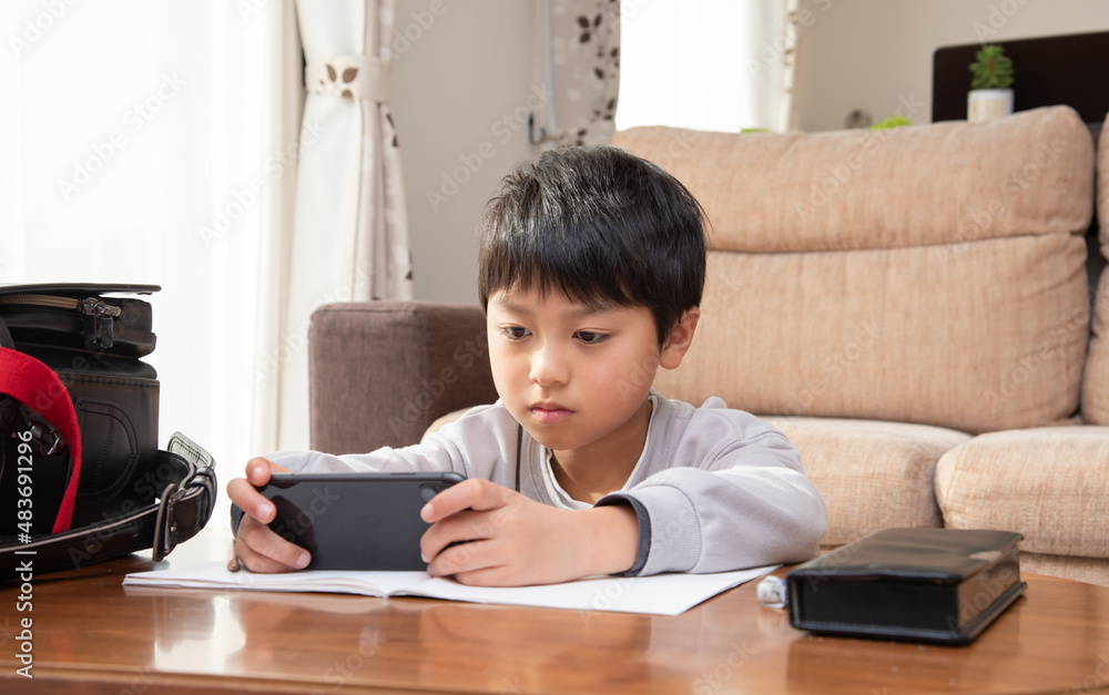 勉強中にスマホを見る小学生の男の子 勉強中にスマホを見る小学生の男の子