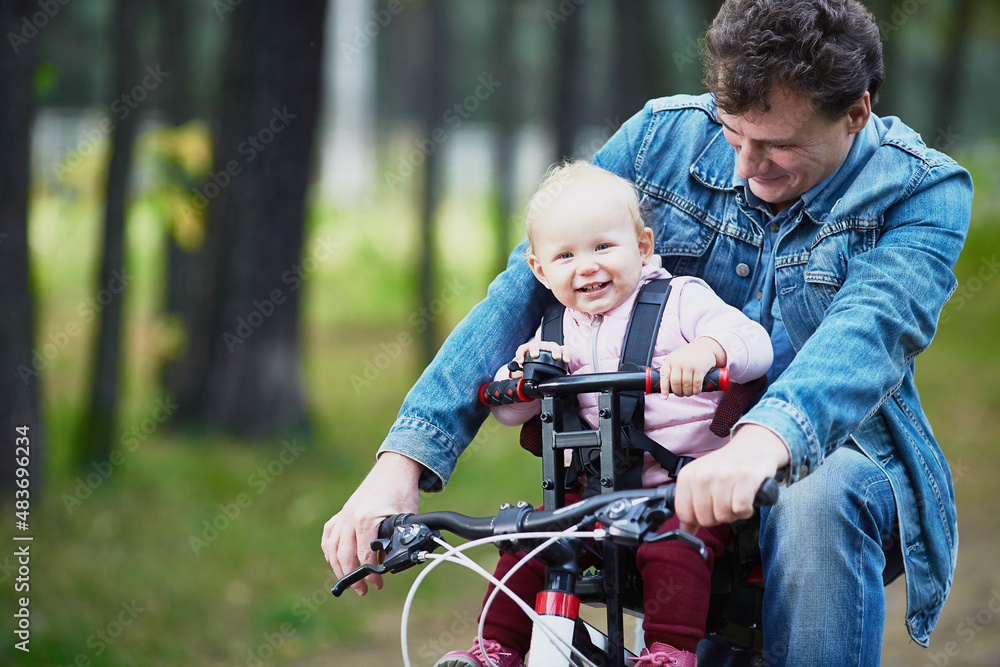 Dad and a small child ride a bicycle in the summer through the forest using a bicycle chair for children Dad and a small child ride a bicycle in the summer through the forest using a bicycle chair for children