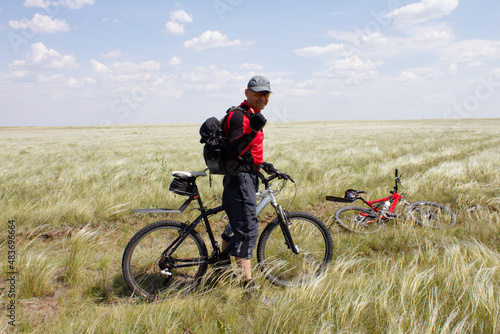 Smiling man with his bicycle stands in the steppe, overgrown with feather grass. Active leisure concept.