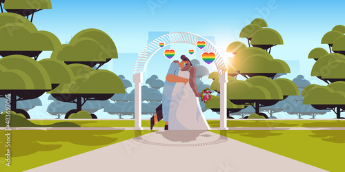 newlywed lesbian couple with flowers kissing near wedding arch transgender love LGBT community wedding celebration