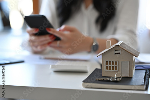 Close up with house model place on white table with businesswoman working as the background.