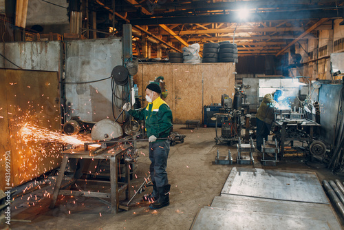 Workers working with metal construction on plant. Metal processing with big angle grinder disk saw and welder welding. Sparks in metalworking at factory.
