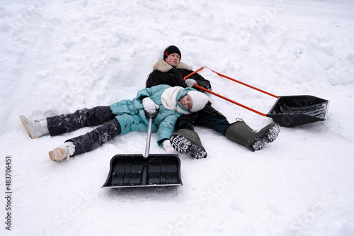 girl and guy in winter clothes are tired and lie resting in  snow in winter. There are big shovels next to them. Rest after snow removal
