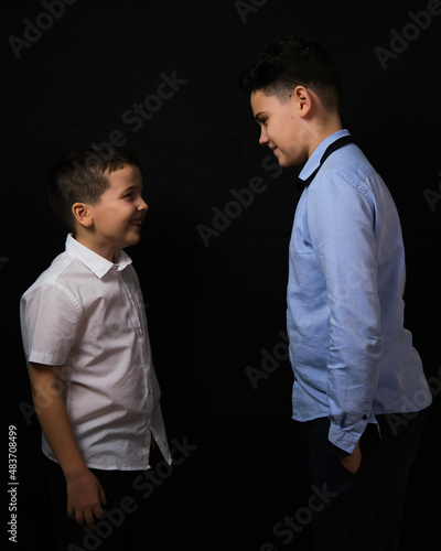 Two boys on a black background are brothers.Senior and junior.Atelier.The younger one laughs at the older one