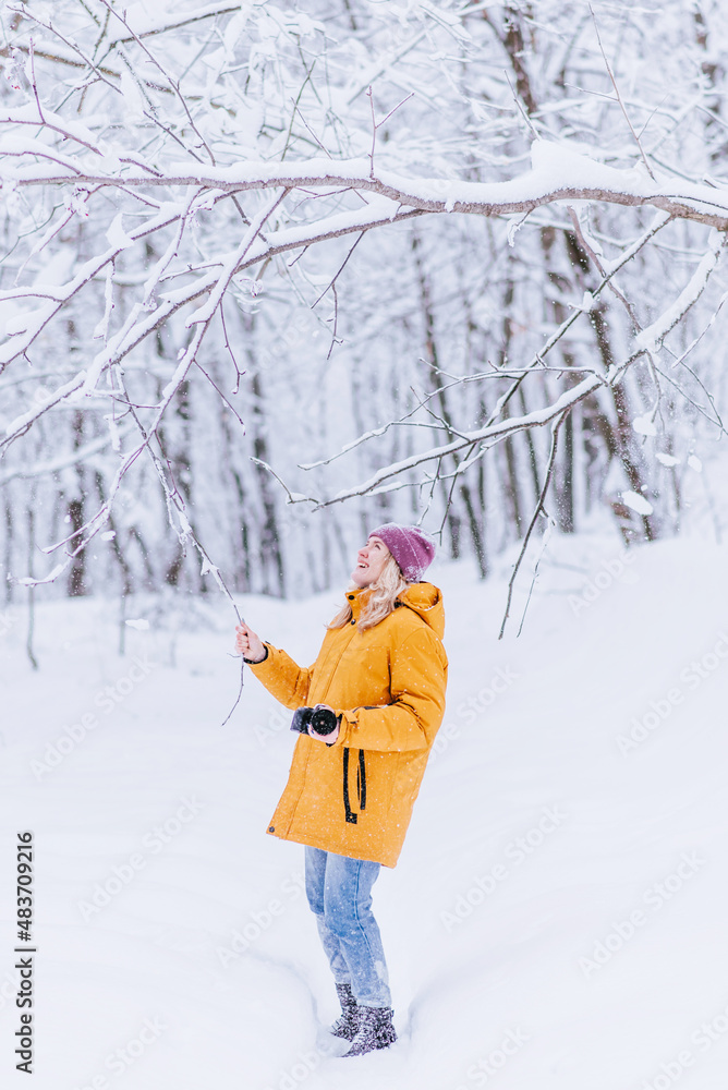 Happy girl photographer in a yellow jacket takes pictures of winter in a snowy park Happy girl photographer in a yellow jacket takes pictures of winter in a snowy park