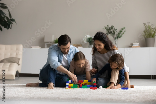 Couple with kids play cubes toys at home  sit on warm floor with underfloor heat system  enjoy playtime leisure and favourite hobby construct together use colourful blocks. Family fun games concept