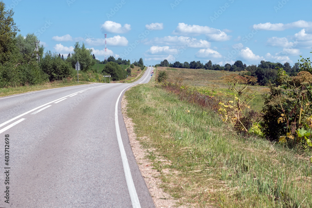 Highway goes along the wooded countryside on a summer sunny day