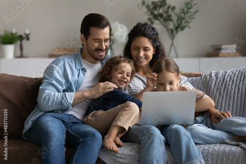 Happy couple with children relaxing on sofa with laptop, watching new blog content of favourite blogger, enjoy new cartoon use subscription-based streaming service. Family leisure, modern tech concept