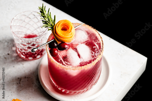 Cranberry orange margarita  on the edge of a counter with an orange peel rose and sprig of rosemary. photo