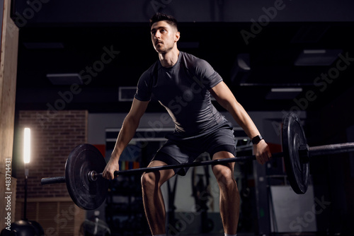 A strong man doing lifting heavy weights at the gym and exercising his biceps.