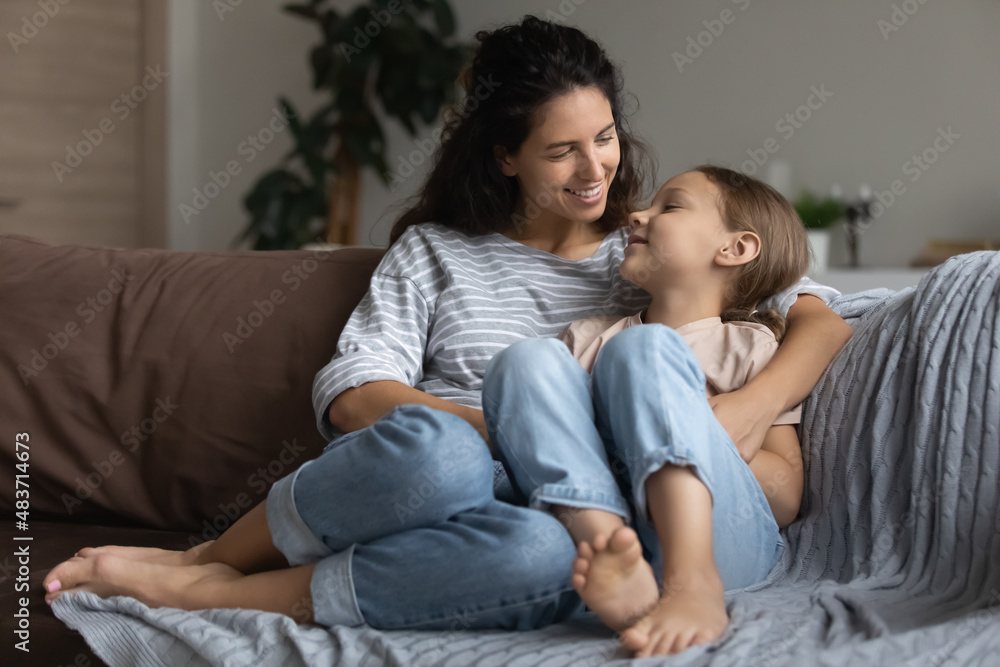 Loving mother cute little 6s daughter share secrets having warm conversation hugging sit together on sofa in cosy living room at home. Motherhood, upbringing, trustworthy relationships, bond concept Loving mother cute little 6s daughter share secrets having warm conversation hugging sit together on sofa in cosy living room at home. Motherhood, upbringing, trustworthy relationships, bond concept