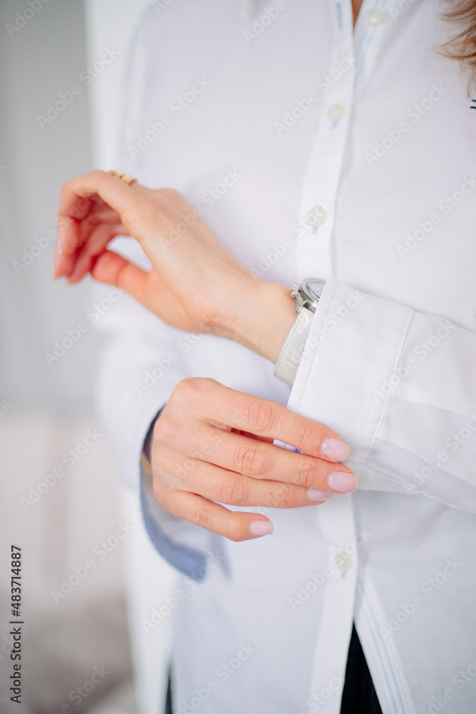 The girl fastens her buttons on the cuffs of her white shirt.