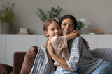 Loving mother cuddling her little cute daughter, family sit on cozy sofa at home smile look at camera enjoy tender moment full of love. Happy motherhood, portrait of caring mom and 5s child concept