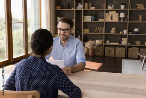 Smiling young male hr manager in eyeglasses holding job interview with female Indian candidate, discussing working experience, feeling satisfied with meeting, copy space, good first impression. photo