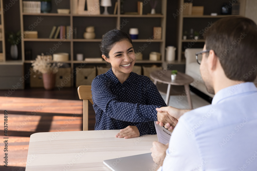 Smiling young Indian female job seeker shaking hands with Caucasian hr manager, starting interview meeting or accepting offer proposal, making good first impression talking in modern office room. Smiling young Indian female job seeker shaking hands with Caucasian hr manager, starting interview meeting or accepting offer proposal, making good first impression talking in modern office room.