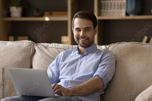 Portrait of handsome young man sitting on couch with computer on laps, enjoying using software applications, working remotely on online project, web surfing information, shopping, tech addiction.