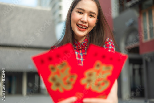 Beautiful Asian woman wearing a traditional red cheongsam on Chinese New Year.Hand holding red envelope or Ang pao with Chinese character means happiness or good fortune.