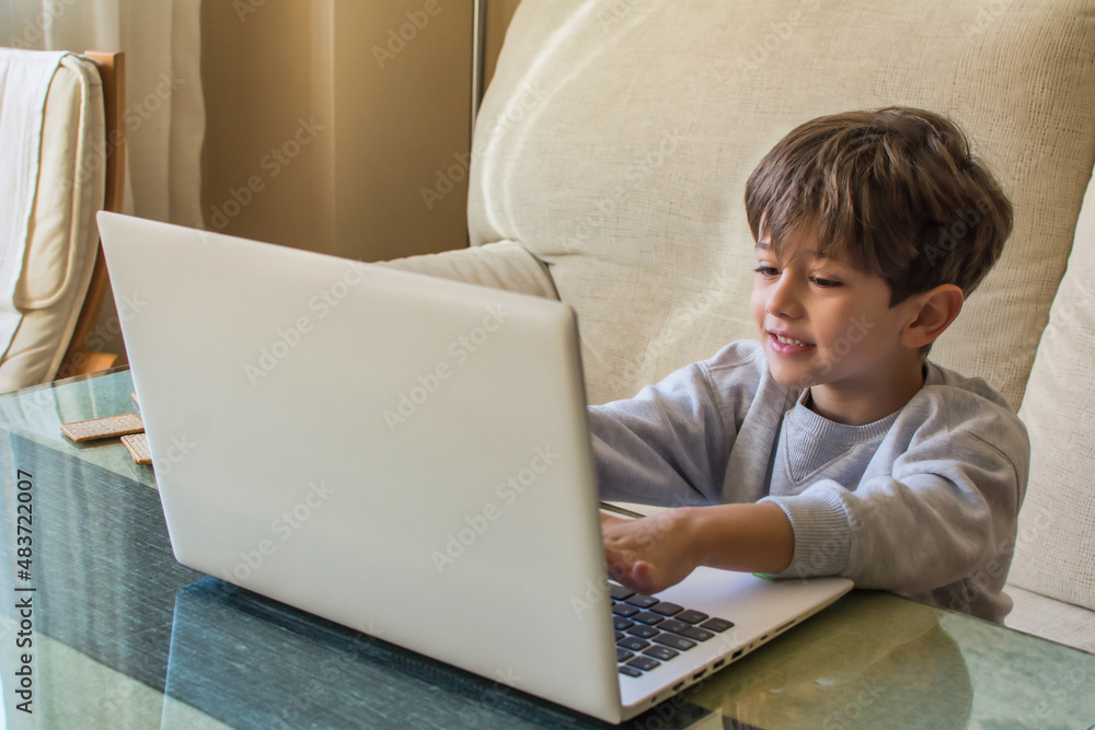 Young Caucasian Boy Using Laptop. Child Using The Laptop In The Living Room At Home And Sitting On The Sofa, He Is In His Pajamas. He Entertains Himself Playing With New Technologies. Lifestyle. Young Caucasian Boy Using Laptop. Child Using The Laptop In The Living Room At Home And Sitting On The Sofa, He Is In His Pajamas. He Entertains Himself Playing With New Technologies. Lifestyle.