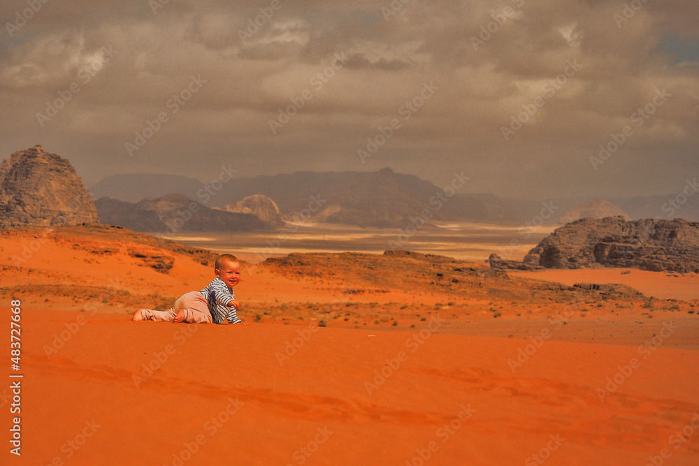 A cute baby girl crawling on a sand. Wadi Rum desert and mountains, Jordan.