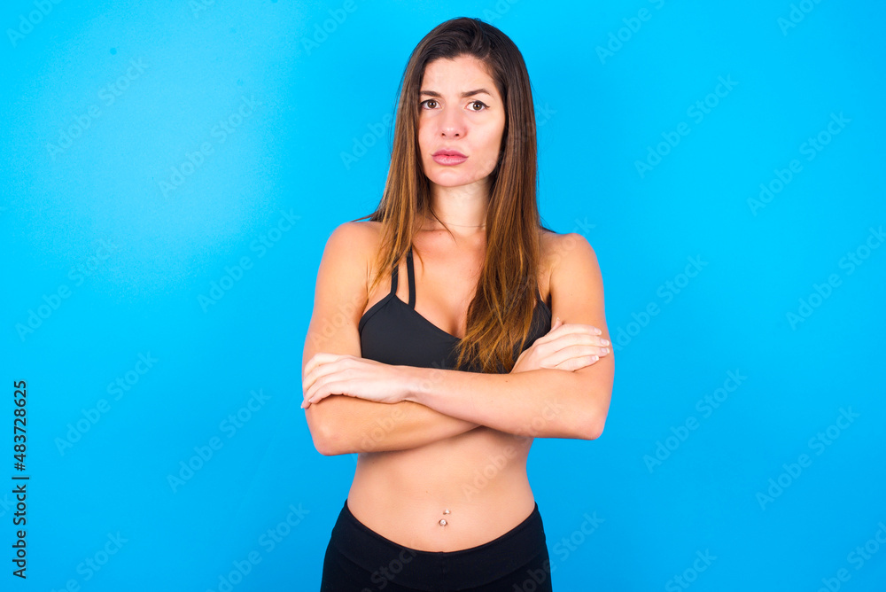 Fototapeta premium Young beautiful sportswoman doing sport wearing sportswear over blue background frowning his face in displeasure, keeping arms folded, waiting for an explanation.