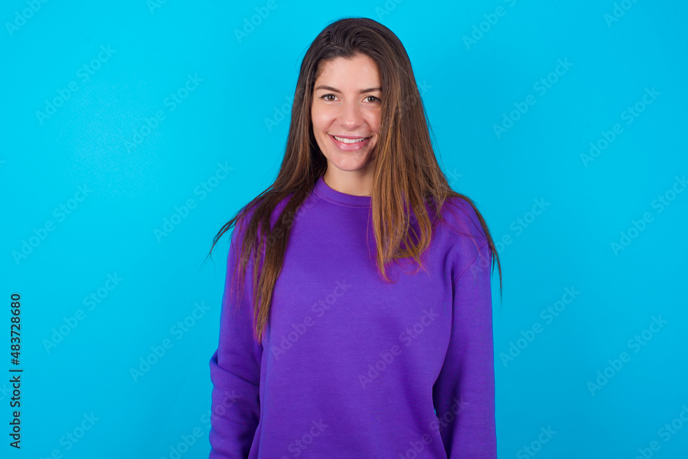 Fototapeta premium young caucasian woman wearing purple hoodie against blue background with nice beaming smile pleased expression. Positive emotions concept
