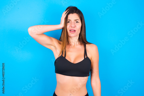 Portrait of confused Young beautiful sportswoman doing sport wearing sportswear over blue holding hand on hair and frowning, panicking, losing memory. Worried and anxious can not remember anything.