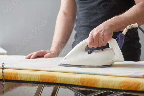 Men's hands hold a white iron and iron on the ironing board. Close-up. Faceless. Copy space. Domestic duties are performed by men