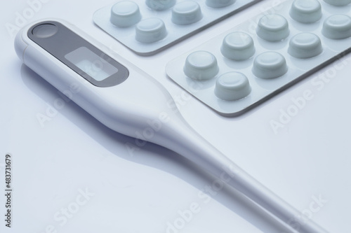 tablets in a package and a white electronic thermometer on a white surface close-up.