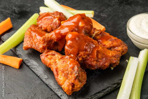 BBQ wings. American recipe for buffalo wings in red sauce with vegetables cut into sticks, dark table.