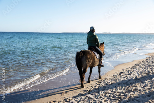 Eine junge Frau reitet mit ihrem Pferd nahe der Brandungslinie am Strand entlang