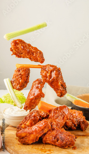 Falling chicken wings buffalo sauce with carrot and celery sticks. Fried bbq wings in flight. Traditional American cuisine concept.