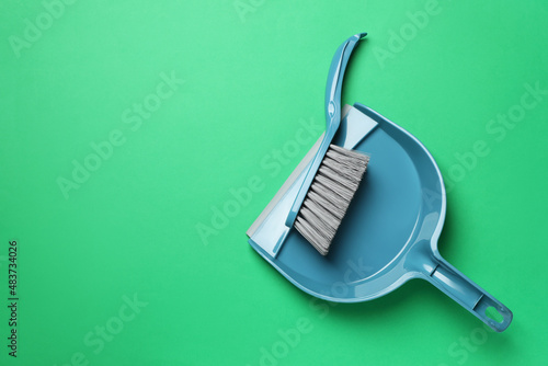 Plastic hand broom and scoop on green background, flat lay. Space for text photo