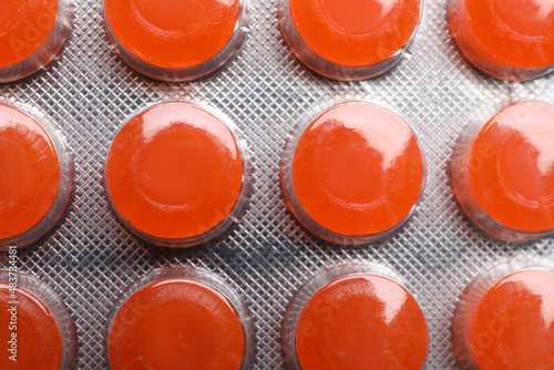 Blister with orange cough drops as background, closeup