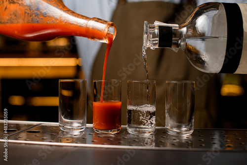 Bartender pouring tequila and tomato juice into small glasses on bar.