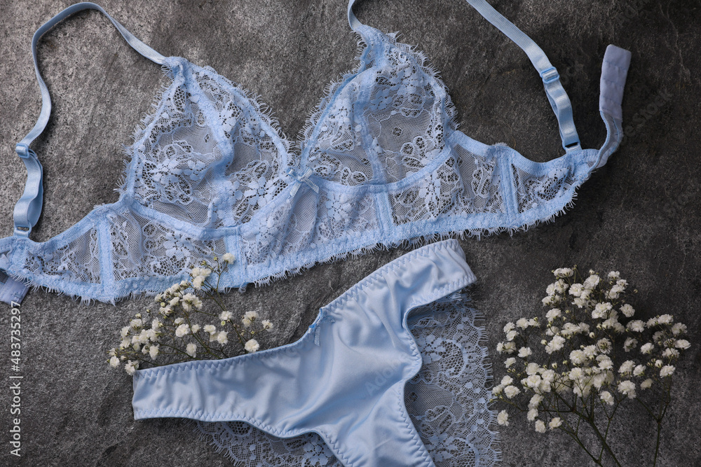 Elegant light blue women's underwear and gypsophila flowers on grey background, flat lay