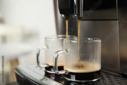 Espresso machine pouring coffee into glass cups against blurred background, closeup. Space for text
