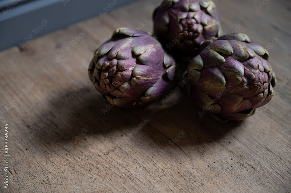 Fototapeta premium three fresh artichokes lie on a rustic wooden board asl healthy food