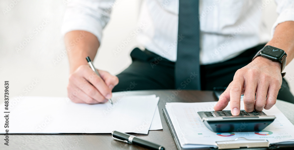 Business man using calculator to calculate profit, income, investment budget in business and writing note. Sitting at office. Business man using calculator to calculate profit, income, investment budget in business and writing note. Sitting at office.