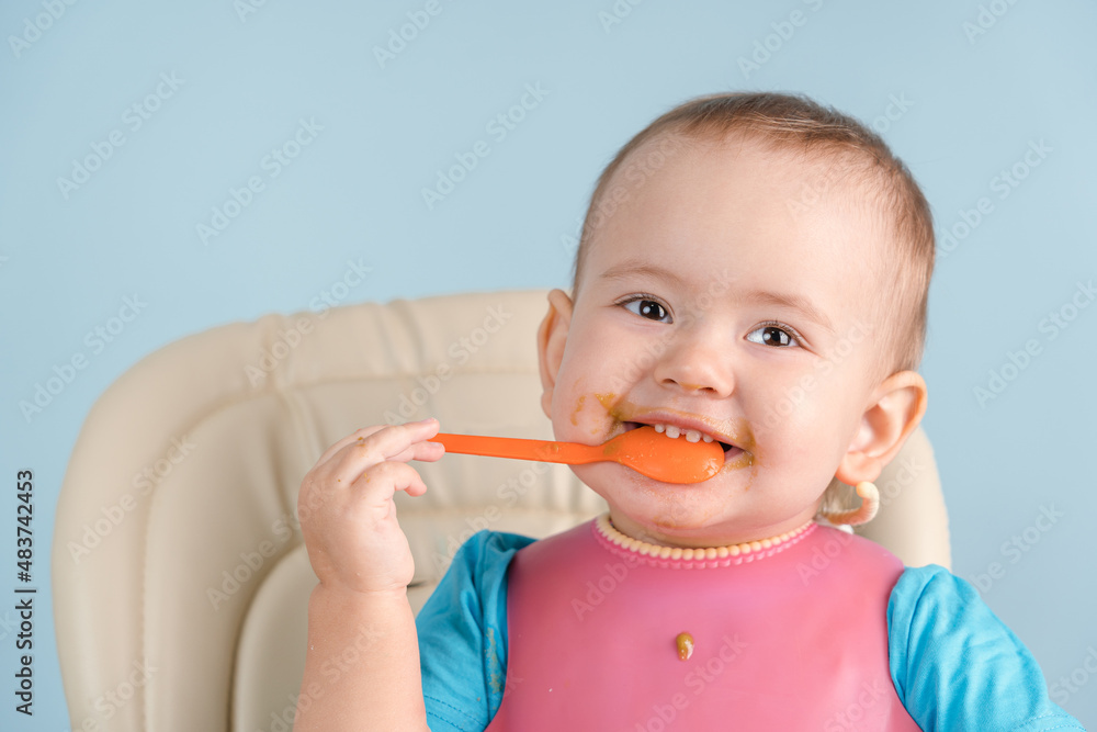 smiling grimy newborn 12-17 months old in a pink bib puts a spoon in his mouth and nibbles it with his teeth smiling grimy newborn 12-17 months old in a pink bib puts a spoon in his mouth and nibbles it with his teeth